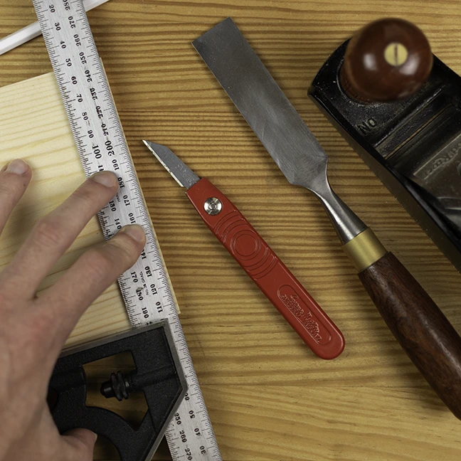 Using hand tools to square the end of a piece of pine Using a combination square and a marking knife to square the end of a piece of pine.